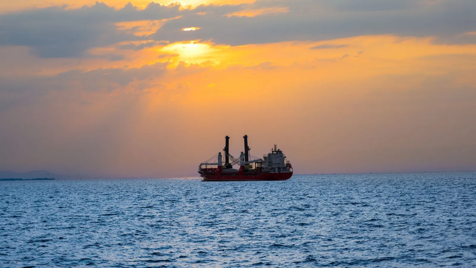 A general cargo ship silhouetted on calm water against an orange sunset — file stock photo, not one of the vessels attacked in the Black Sea, no people visible
