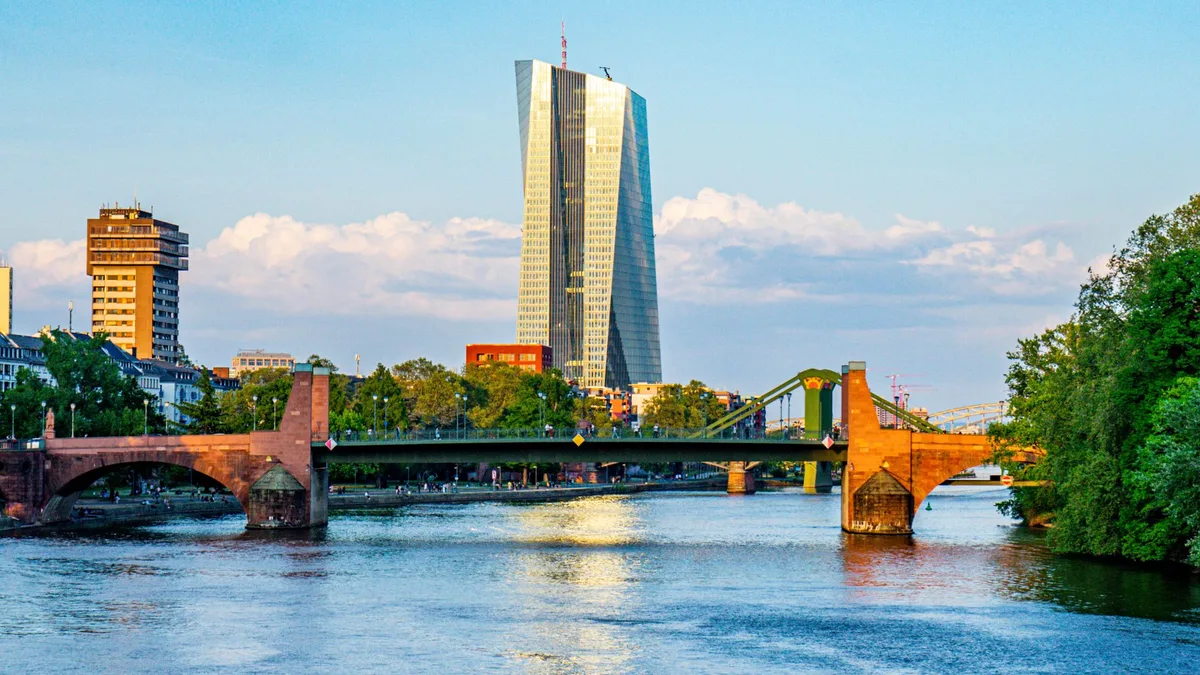 The European Central Bank's glass tower in Frankfurt rising behind the Alte Brücke over the River Main on a sunny evening — file stock photo from May 2022, distant passers-by, none identifiable