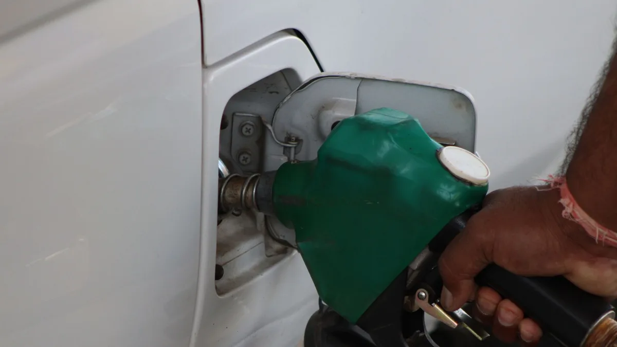 Close-up of a hand holding a green fuel nozzle while refuelling a white car — file stock photo, not taken in the EU for this story, no identifiable people