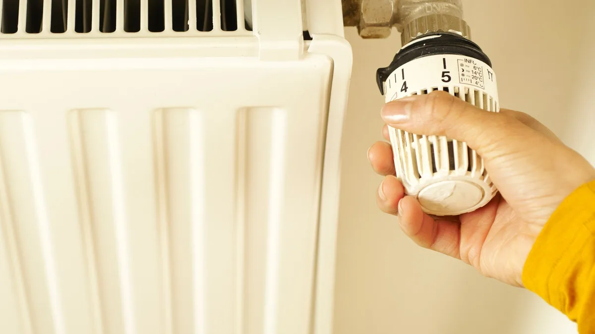 A hand turning the thermostatic valve on a white home radiator — file stock photo from 2022, face not shown