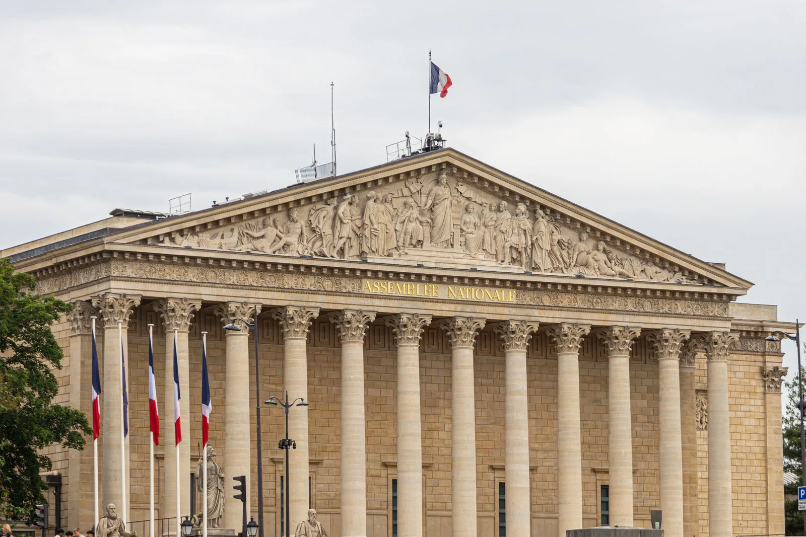 The neoclassical facade of the Palais Bourbon in Paris, home of the French National Assembly, with French flags and the gold Assemblée nationale lettering, no people