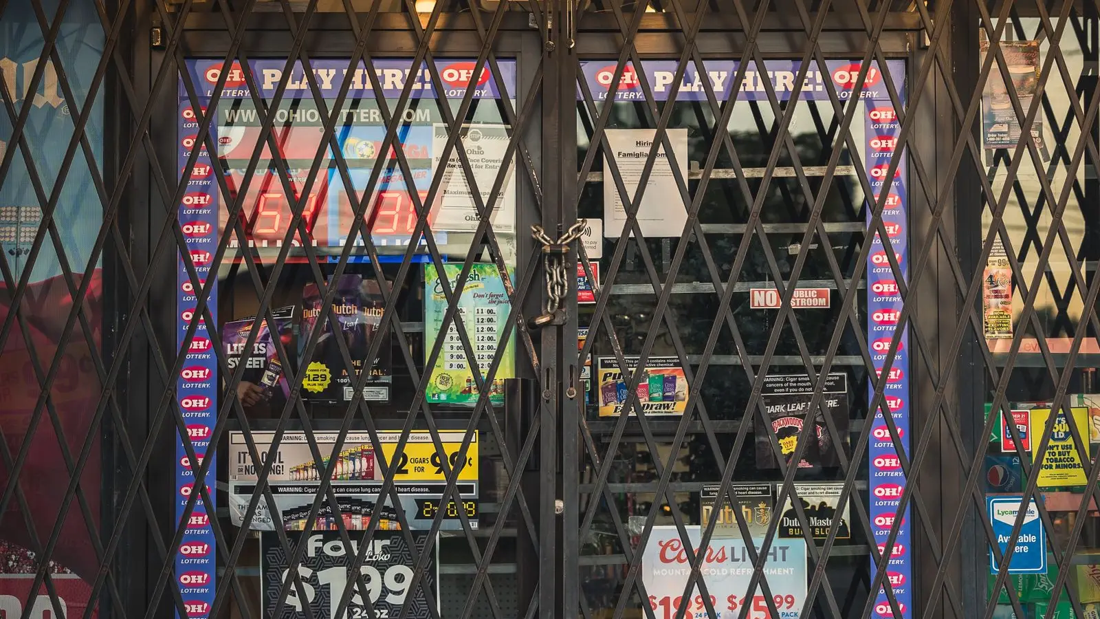 A closed shop front behind a locked, chained metal security grille, posters visible through the glass — file stock photo taken in the United States, not in France, no people