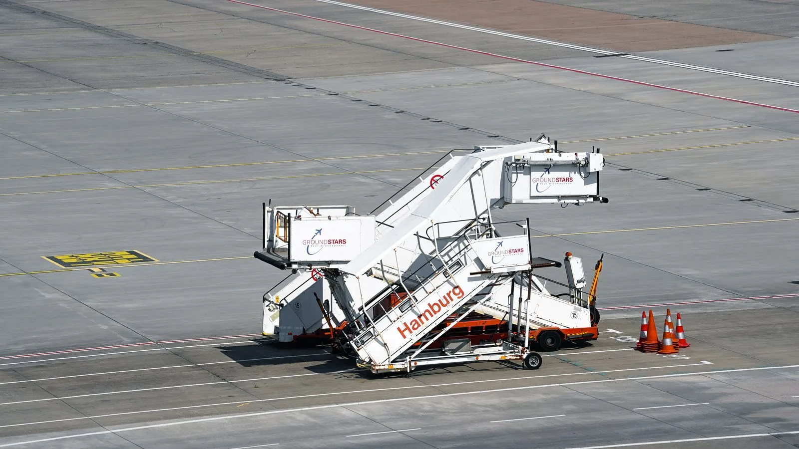 Empty white passenger boarding stairs parked on the apron at Hamburg Airport, with orange traffic cones and no aircraft or people; file stock photo, not a deportation flight