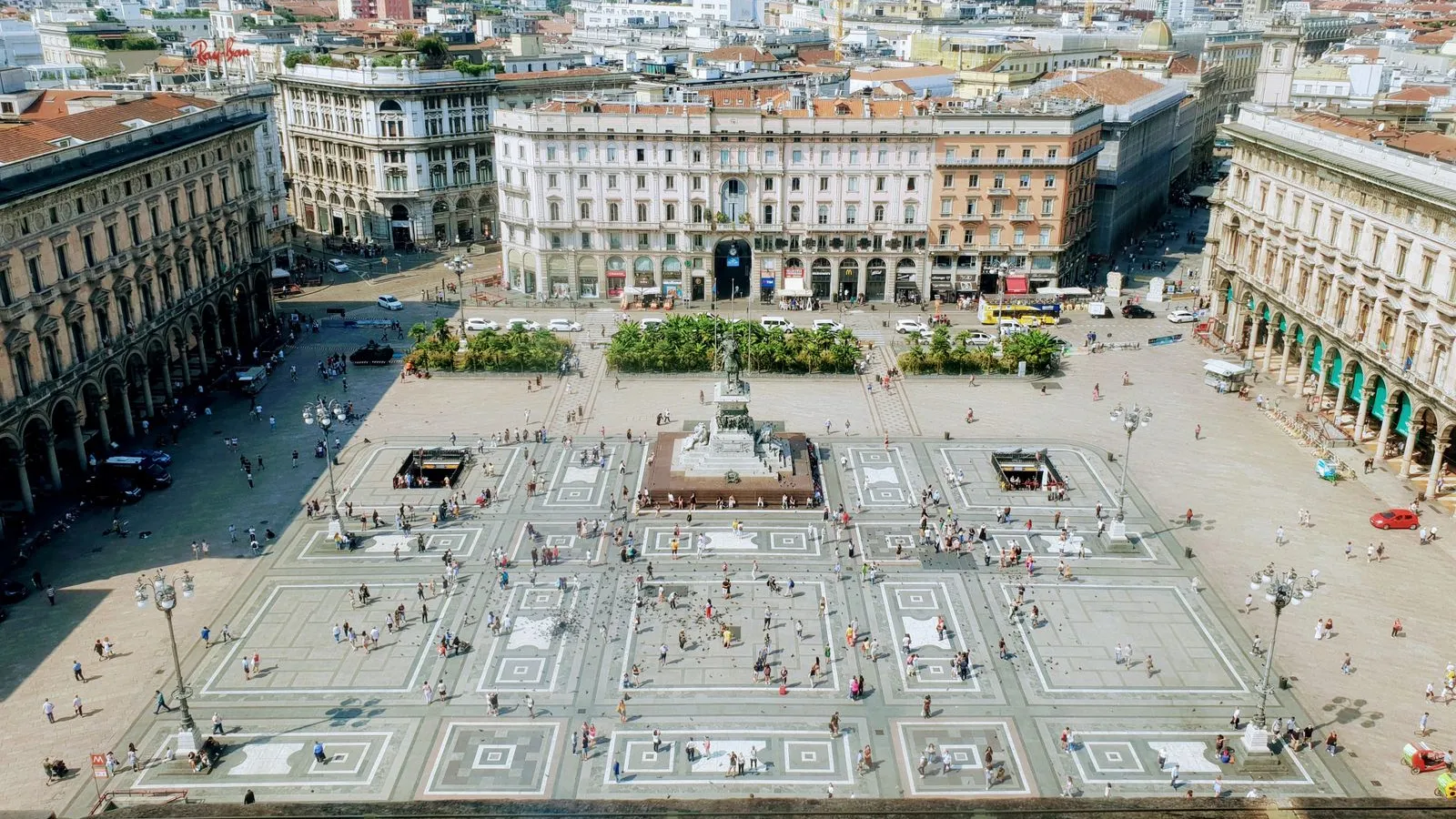 Aerial view over Piazza del Duomo in Milan on a summer day, with the equestrian statue at its centre and the arcades of the Galleria on the left — file stock photo taken in 2020, not during the October 2026 protests, no identifiable people