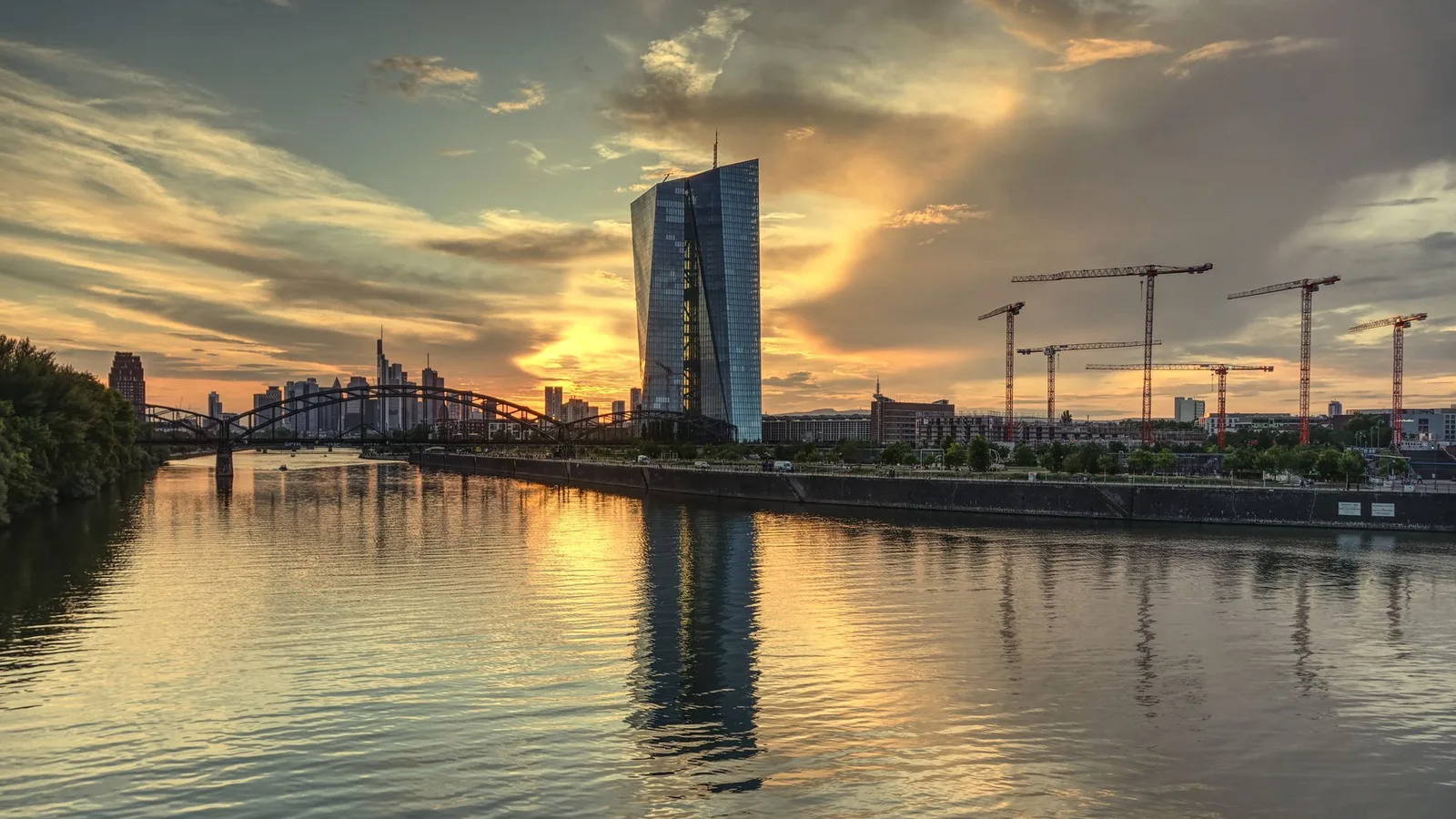 The European Central Bank's glass tower in Frankfurt reflected in the River Main at sunset, with construction cranes and the city skyline behind; file stock photo, not taken on the day of the announcement