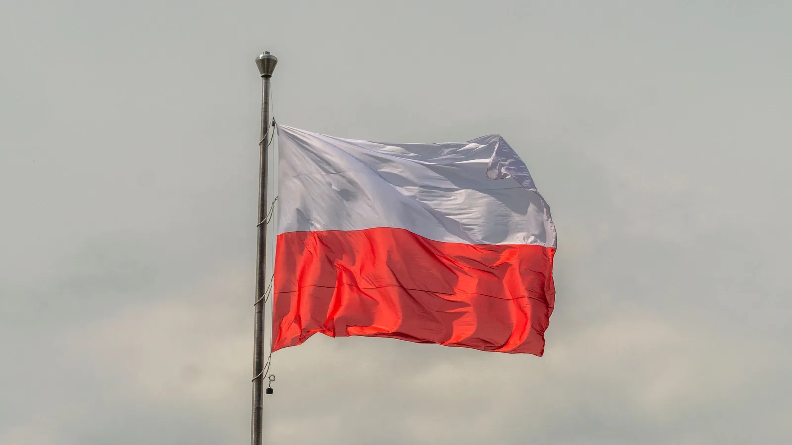The white and red Polish national flag flying from a flagpole against a grey cloudy sky; file stock photo, not taken at the Constitutional Tribunal