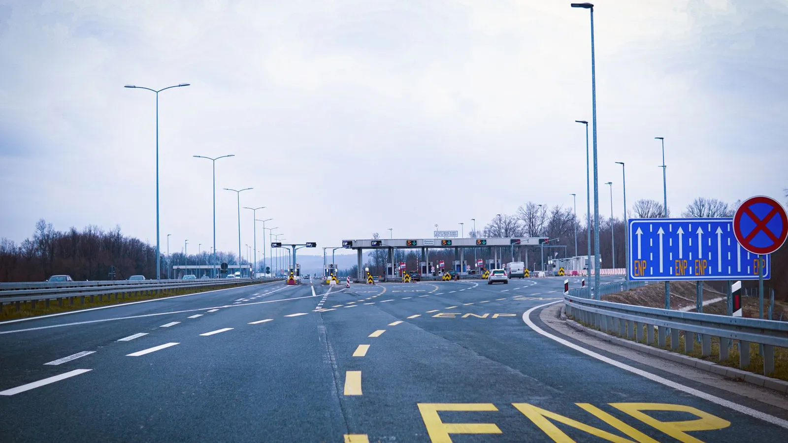 A wide motorway leading to a row of toll booths under a grey sky — file stock photo of a toll plaza, not a Schengen border checkpoint; vehicles distant, no identifiable people