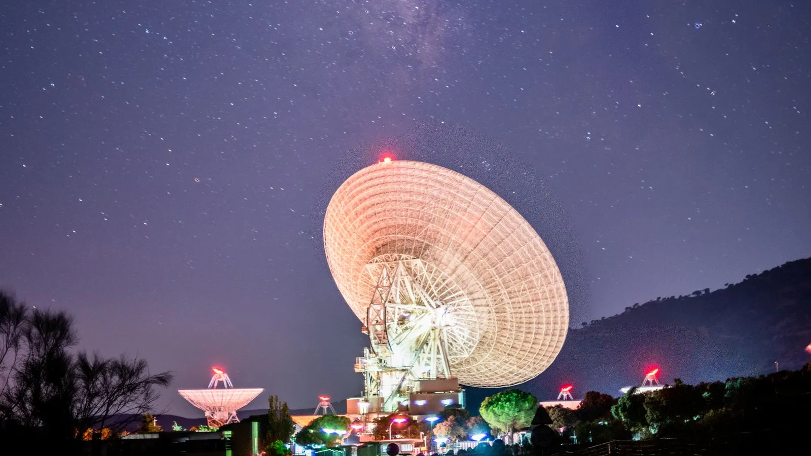 A large radio antenna dish lit up at night under a starry sky with the Milky Way — file stock photo, not a Starlink, Govsatcom or IRIS² facility, no people